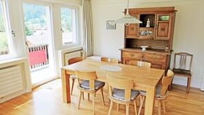 Una sala da pranzo con tavolo e sedie in legno, un mobile contenitore con cassetti e vista attraverso ampie finestre.