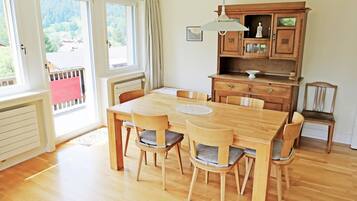 Une salle à manger avec une table et des chaises en bois, un buffet avec des tiroirs et une vue dégagée sur l’extérieur grâce à de grandes fenêtres.