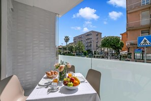 Ein Balkon mit Frühstückstisch, einer Obstschale, einer Blumenvase und Blick auf die Stadt.