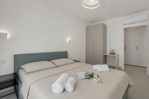 Ein modernes Hotelzimmer mit einem ordentlich bezogenen Bett, einem Nachttisch, einem kleinen Seitentisch mit einem Korb und einem Kleiderschrank.