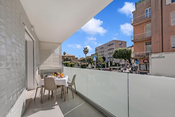 Ein Balkon mit Tisch und Stühlen, Blick auf die Straße und Gebäude im Hintergrund.