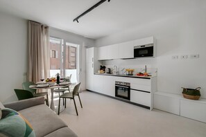 Eine moderne Küche mit weißen Schränken, einer Mikrowelle und einem Backofen. Es gibt eine Essecke mit einem Tisch für zwei Personen und ein Sofa im Vordergrund.