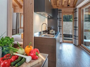 A modern kitchen with a wooden ceiling, a large window, and a view of a stone wall outside. - Turrabuel Appartement/Fewo Turrabuel 3-Zimmer Deluxe by Interhome (Parpan)
