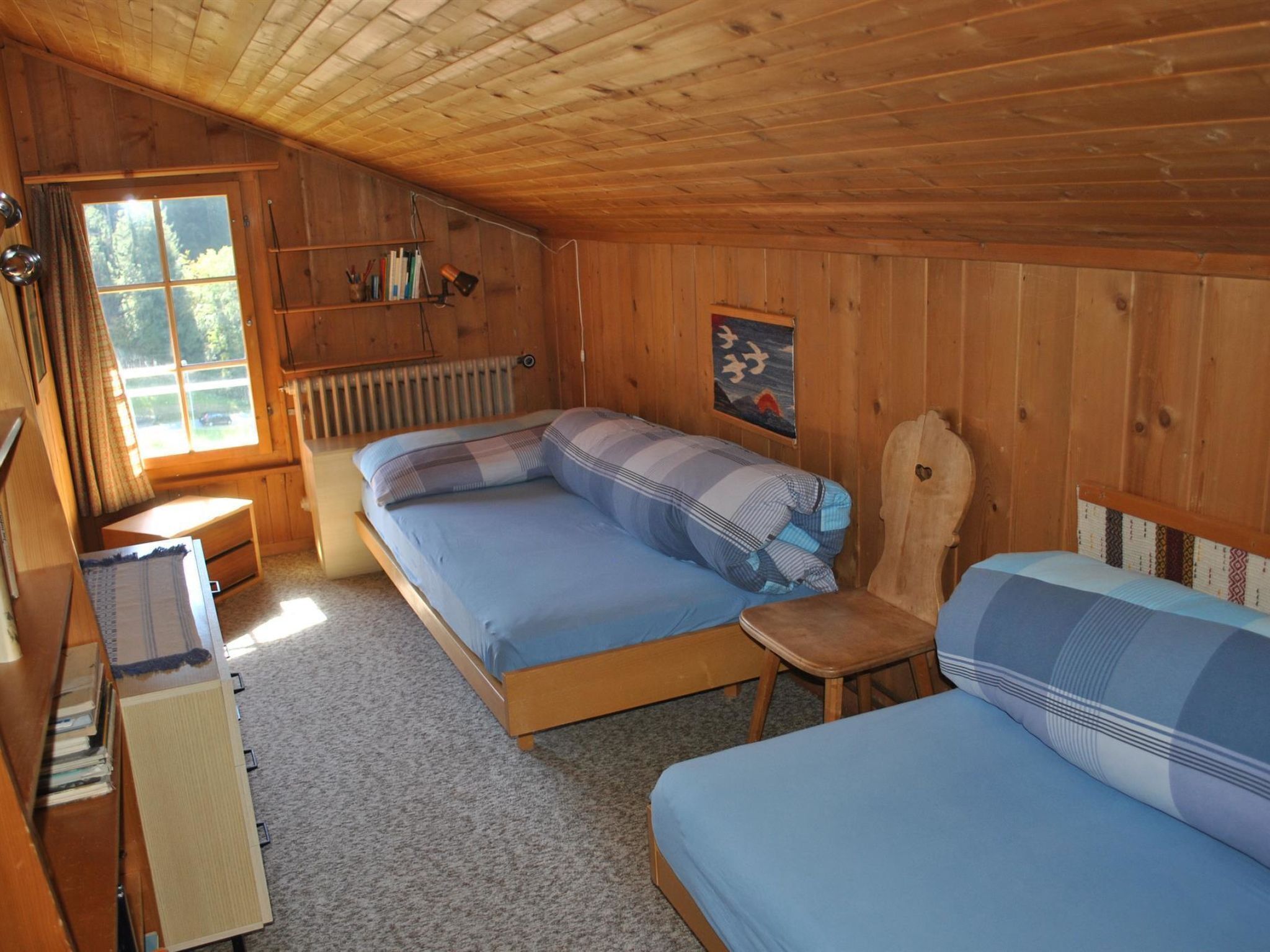 Une chambre dans un chalet en bois, avec deux lits, un bureau, un radiateur et une fenêtre avec des rideaux.