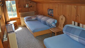 Een houten kamer met twee bedden, een bureau, een radiator en een raam met gordijnen.