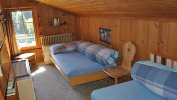Une chambre dans un chalet en bois, avec deux lits, un bureau, un radiateur et une fenêtre avec des rideaux.