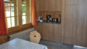 Een keuken met houten kastjes, een aanrecht met apparatuur, een raam met gordijnen en een radiator.
