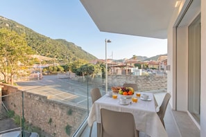 Ein Balkon mit Frühstückstisch, ein Tennisplatz und eine Bergkulisse im Hintergrund.