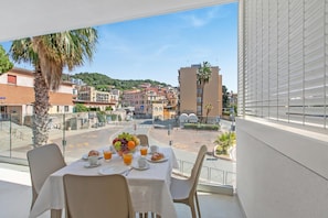 Ein Balkon mit Frühstückstisch, Blick auf eine Stadtlandschaft mit Gebäuden und wolkenlosem Himmel.