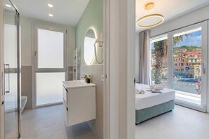 Ein modernes Hotelzimmer mit einem großen Bett, einem Badezimmer mit Spiegel und Waschbecken sowie Blick auf eine Stadt durch das Fenster.
