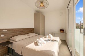 Quarto de hotel moderno com uma cama grande, uma mesa de cabeceira, uma mesinha de apoio, um porta-toalhas, uma revista, uma tigela e uma porta de vidro deslizante para o exterior.