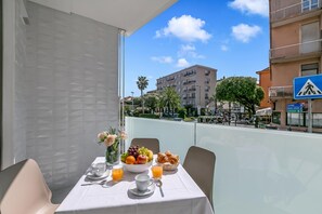 Mesa de varanda com itens de café da manhã, vista desimpedida da rua e um edifício com varandas.