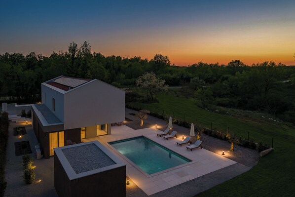 Ein modernes Haus mit Swimmingpool, Sitzgelegenheiten im Freien und Blick auf den Sonnenuntergang.