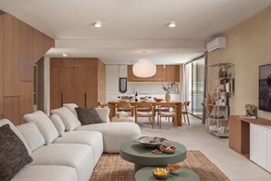 Un salon moderne avec un canapé d’angle, un coin repas avec une table en bois et une cuisine en arrière-plan.