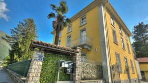 A yellow building with a stone entrance, a metal gate, and a small balcony. - Maroggia Apt 2 Near The Lake for 5, Maroggia, Switzerland (Maroggia)