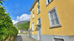 A yellow building with a cobblestone path, a gate, and a mountain in the background. - Maroggia Apt 2 Near The Lake for 5, Maroggia, Switzerland (Maroggia)