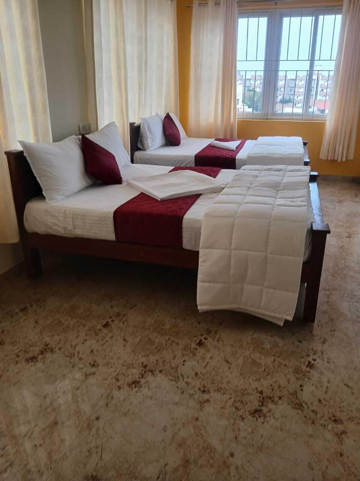 Una habitación de hotel con dos camas, vista a edificios por la ventana y piso alfombrado.