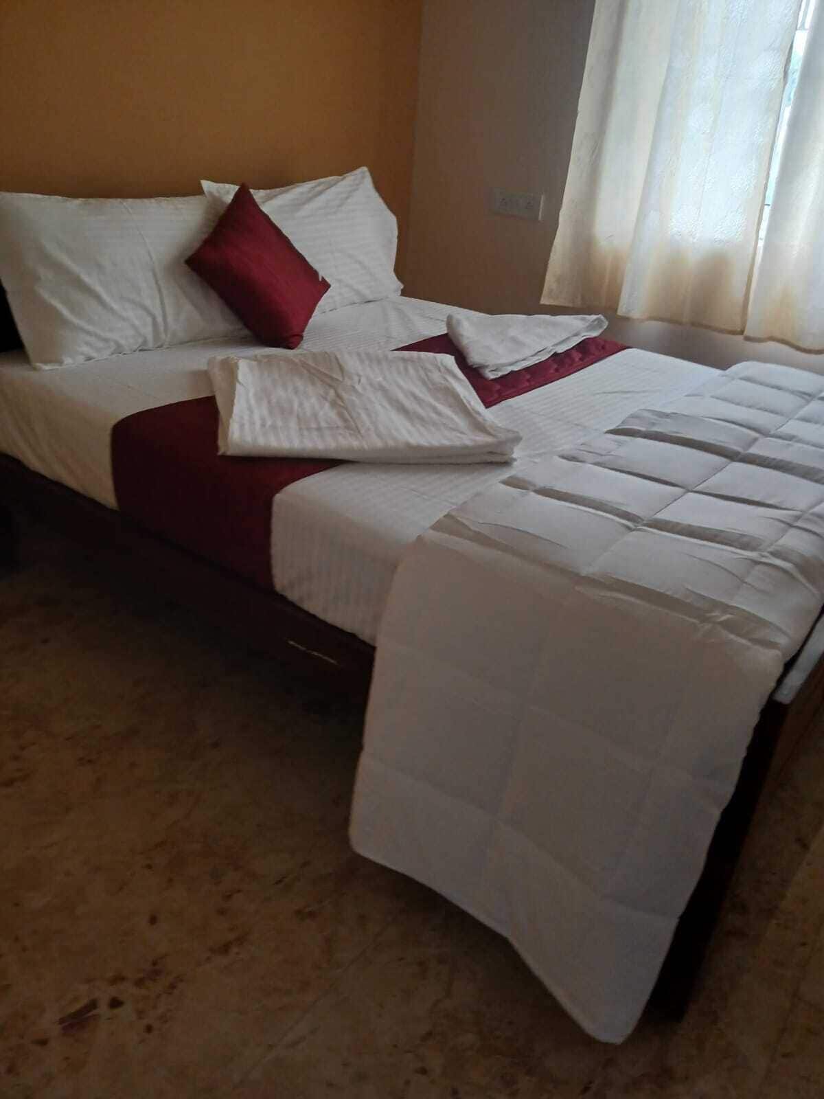 A bed with white bedding, a red pillow, and a folded white blanket.
