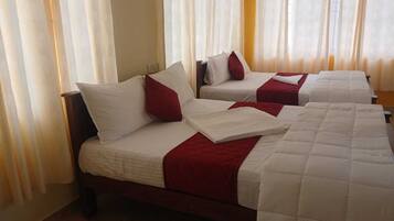 Habitación de hotel con dos camas, cada una con ropa blanca y detalles rojos, y un ventanal con cortinas traslúcidas.
