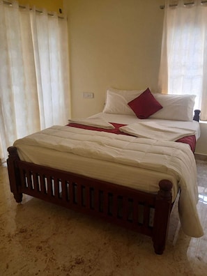 Una cama con estructura de madera, ropa de cama blanca y un almohadón rojo.