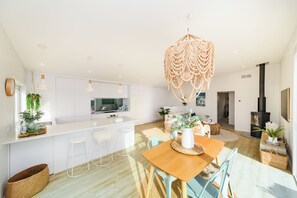 Una cocina moderna con armarios blancos, una isla central, taburetes de bar, una mesa de comedor con sillas y una lámpara colgante.