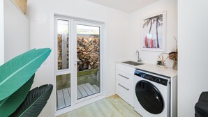 A compact laundry room with a washing machine, a sink, and a glass door leading to a wooden deck. - Stunning 3-bedroom house with the best beach/ocean views (Foxton Beach)