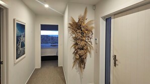 A hallway with a carpeted floor, a wall-mounted decorative plant, a door with a blue panel, and a framed picture on the wall. - Stunning 3-bedroom house with the best beach/ocean views (Foxton Beach)