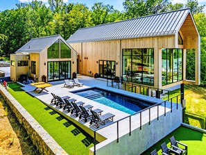 Een modern huis met een groot buitenzwembad, houten gevel en grote ramen.