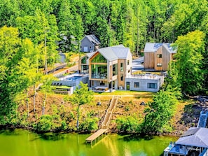 A modern house with a large deck, a swimming pool, and a dock extending into a lake.