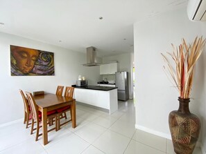 A modern kitchen with white cabinets, a stainless steel refrigerator, and a dining area with a wooden table and chairs.