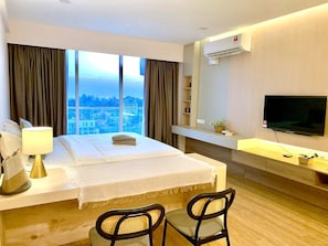 Habitación de hotel con cama, escritorio, silla, televisión y un amplio ventanal con vista a la ciudad.