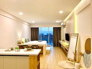 Un cuarto de hotel con cama, escritorio con silla, televisor, ventana grande con cortinas y vista a la ciudad.