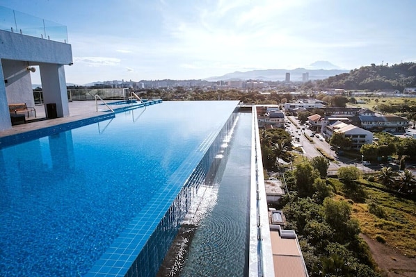 Una piscina infinita en la azotea con vistas a la ciudad, una estructura de edificio moderna y un cielo despejado.