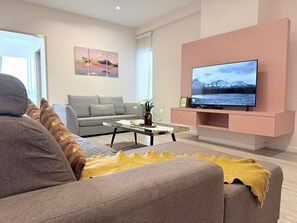 Una sala de estar moderna con un sofá gris, una mesa de centro, un televisor de pantalla plana montado en una pared rosa y un cuadro sobre el televisor.