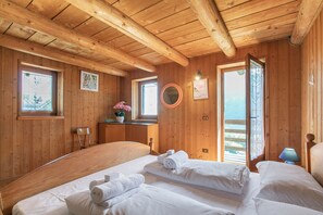 Ein Holzhüttenraum mit zwei Betten, einem Fenster, einem Spiegel und einer Tür, die nach draußen führt.