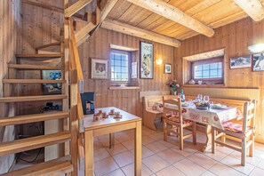 Ein Holzinnenraum mit einem für vier Personen gedecktem Esstisch, einer Treppe und gerahmten Bildern an den Wänden.
