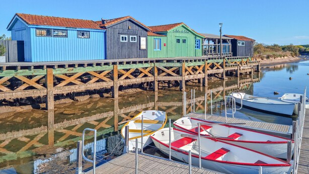 En fastighet vid vattnet med färgglada trähus, en brygga med båtar och en stilla flod.