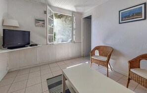 Ein Zimmer mit Fernseher, Korbsesseln, einem Tisch, einem Fenster mit Aussicht und einem gerahmten Bild an der Wand.