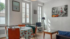 A dining area with a table set for two, a chair, a lamp, and a painting on the wall. - Amazing apartment in La Rochelle with WiFi (La Rochelle)