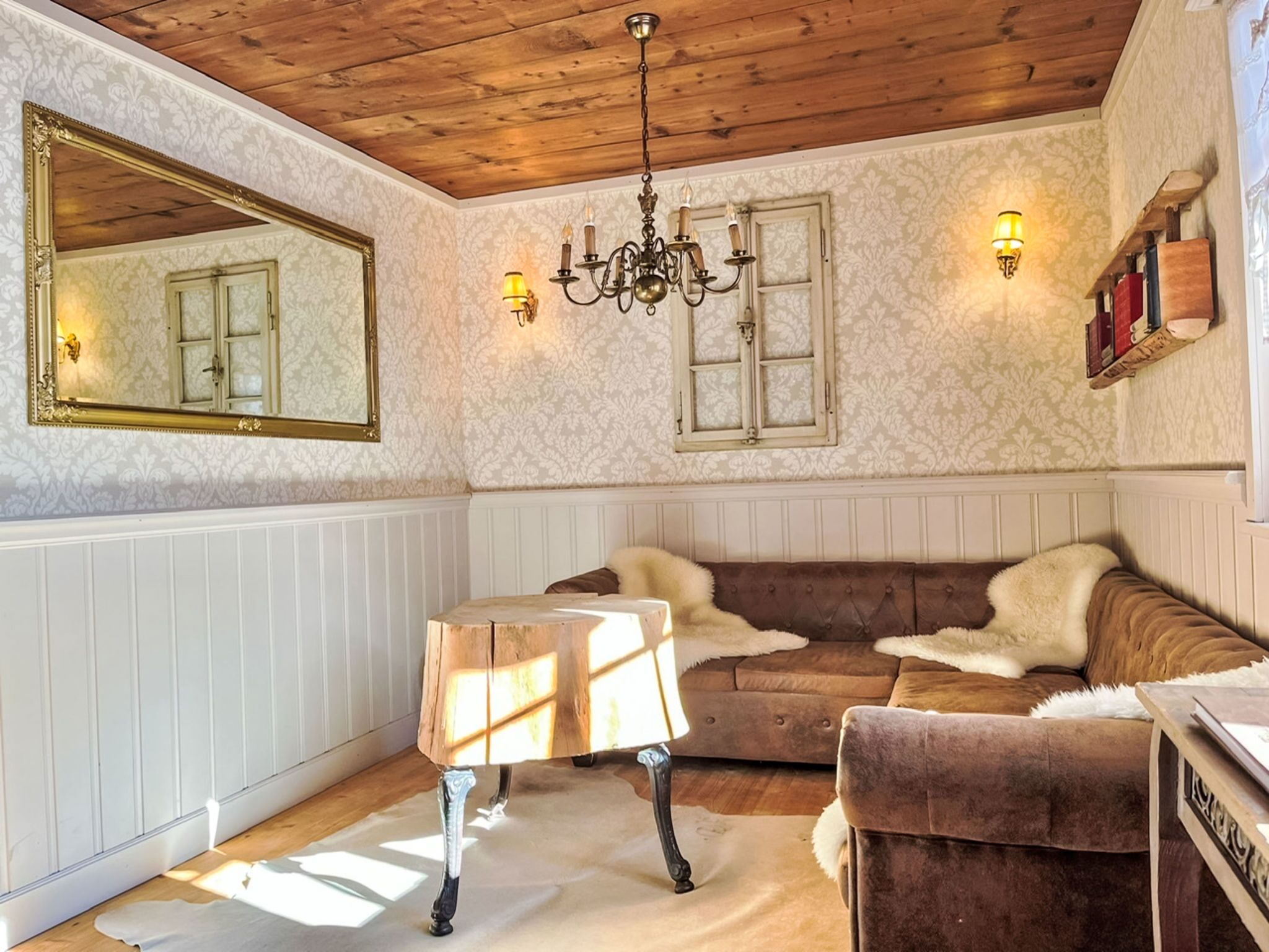 Una habitación con techo de madera, candelabro, espejo, sofá, mesa y luces fijadas a la pared.