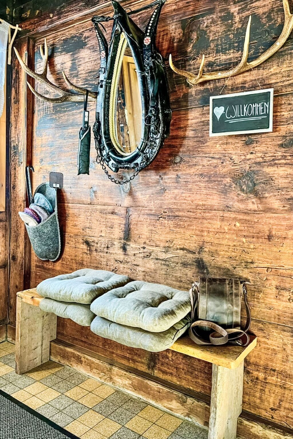 A rustic wooden room with a bench, a saddle, and antlers on the wall.