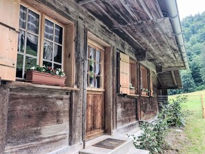 Ein rustikales Holzhaus mit zahlreichen Fenstern, einige mit Fensterläden, und einem kleinen Veranda-Bereich.