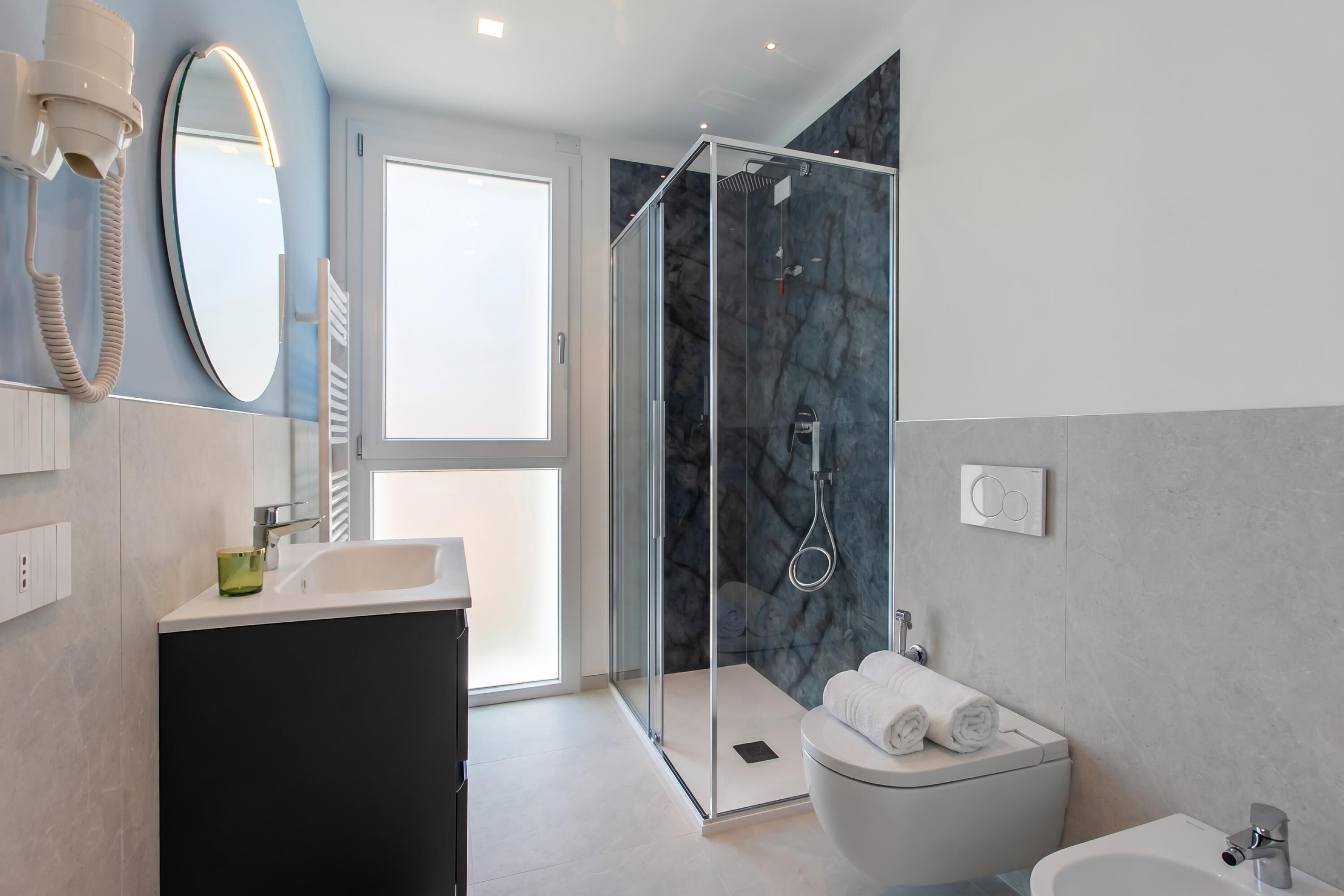 Ein modernes Badezimmer mit einer gläsernen Duschkabine, einem weißen Waschbecken und einer Toilette.