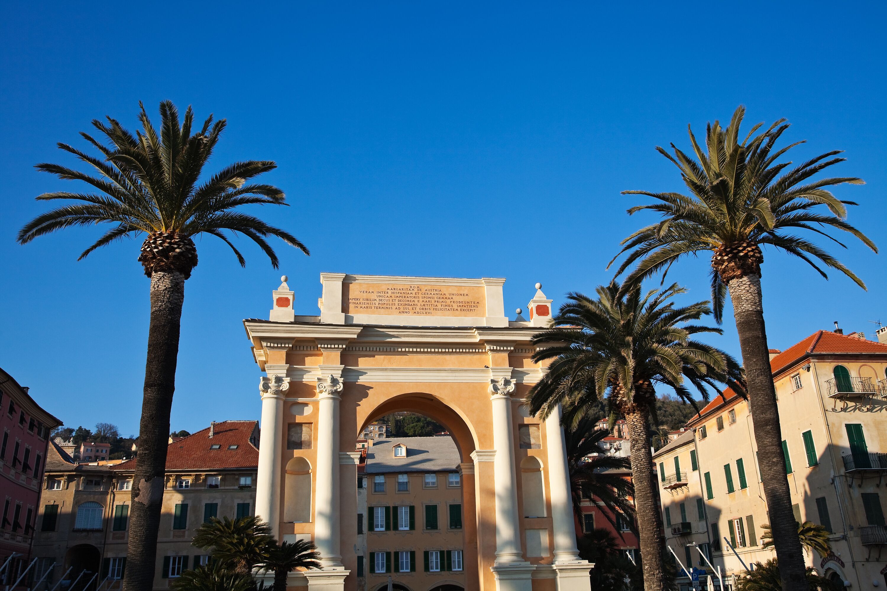 An archway with a plaque, surrounded by palm trees and buildings.