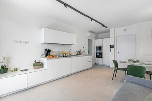 Eine moderne Küche mit weißen Schränken, ein Essbereich mit einem grünen Stuhl und ein graues Sofa.