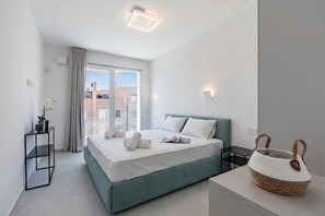 A modern hotel room with a bed, a bedside table, a lamp, a window with curtains, and a view of buildings outside. - Nua Boutique Apartaments 19 Towncentre, Finale Ligure, Italy (Finale Ligure)