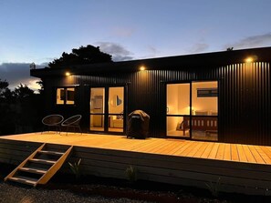 A modern house with a wooden deck, large windows, and a covered barbecue area. - The Cabin & Sauna @ The Highlands (Waipu)