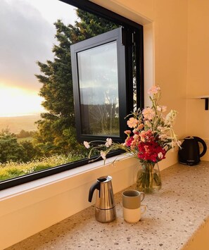 A kitchen counter with a coffee maker, a mug, and a vase with flowers. - The Cabin & Sauna @ The Highlands (Waipu)