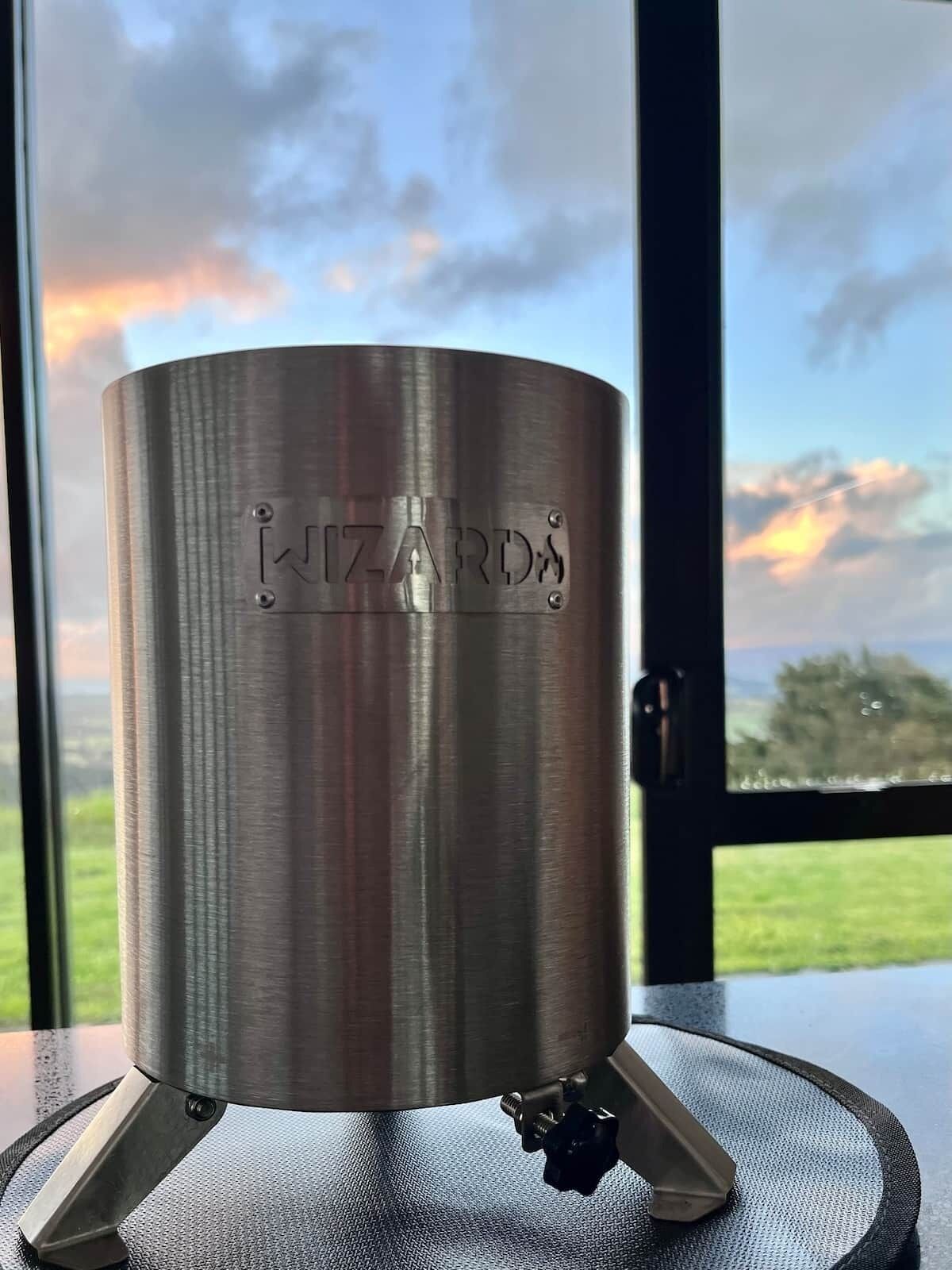 Un objet cylindrique métallique, portant l’inscription « WIZARDS » sur une surface texturée, est placé sur un socle devant lequel on aperçoit une fenêtre.