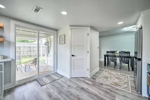 Una habitación con puerta corrediza de vidrio que da a un patio trasero, un comedor con mesa y sillas, y una cocina con refrigerador.